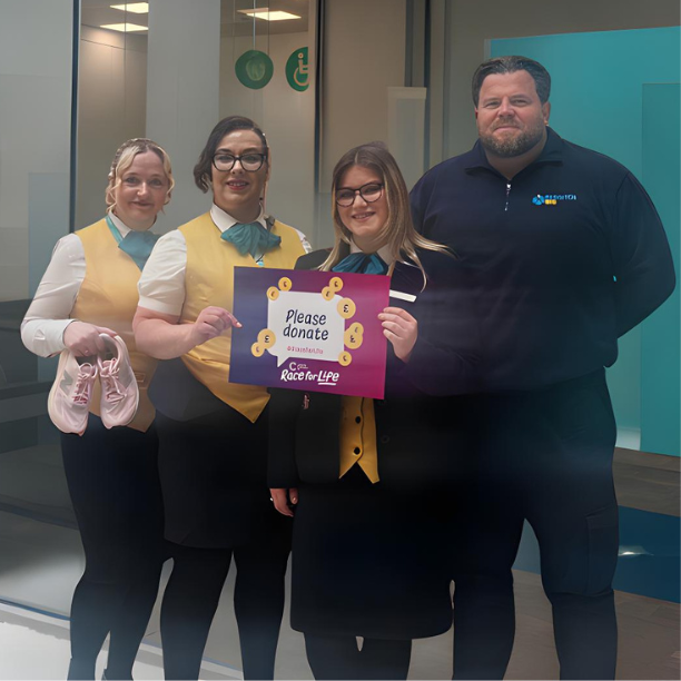 A group of staff from kingfisher in their yellow uniforms, holding a sign to donate for Race for Life.